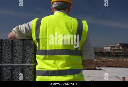 grey haired middle aged man wearing high vis vest and hard hard health and safety  on building construction site in northern ireland uk united kingdom Stock Photo