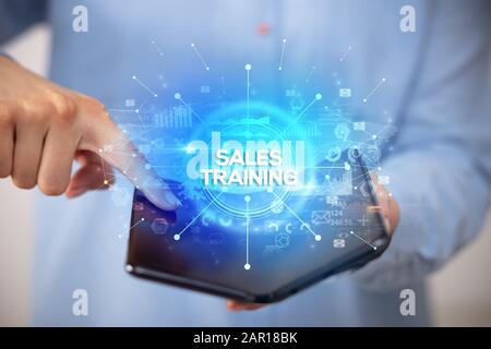 Businessman holding a foldable smartphone with SALES TRAINING inscription, new business concept