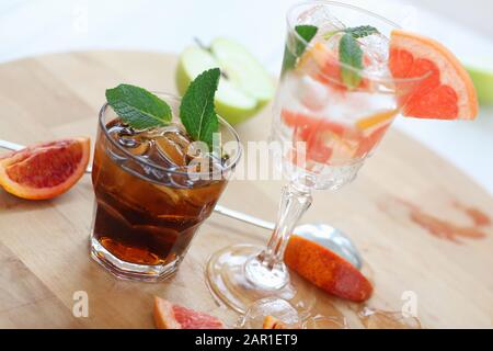 Two cocktails of whiskey with cola and grapefruit with ice vodka and mint. On a wooden board, fragments of fruit are flung up. Photo with depth of Stock Photo