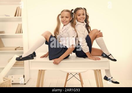 Schoolgirls friends sit on desk. Best friends relaxing. Schoolgirls tidy hairstyle relaxing having rest. School uniform. Rebellious spirit. School club. Little schoolgirls classmates friendly kids. Stock Photo