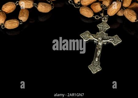 Close-up of an old silver crucifix with Jesus Christ and wooden rosary bead on a black background with reflections Stock Photo