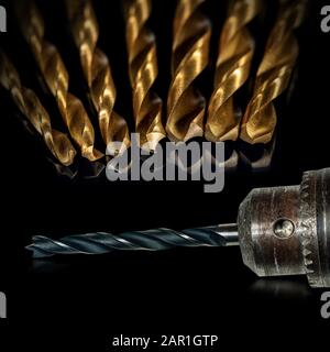 Extreme close-up of an electric drill with black and golden tips on a black background with reflections Stock Photo