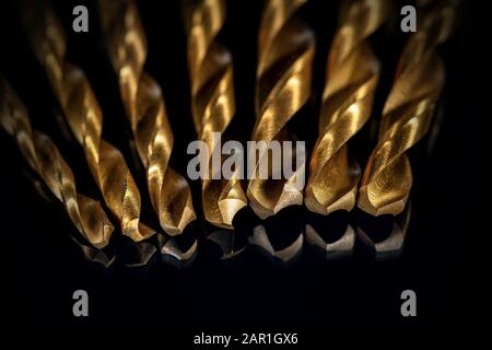 Extreme close-up of a set of golden drill tips on a black background with reflections, selective focus Stock Photo