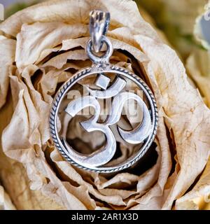 Sterling silver pendant in shape of om symbol in cyrcle placed on dried rose Stock Photo