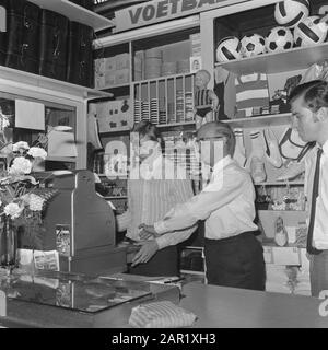 Johan Cruijff in his sports store  Johan Cruyff behind the checkout, all right Henny Cruyff Date: August 8, 1968 Location: Amsterdam, Noord-Holland Keywords: group portraits, sports stores Personal name: Cruyff, Henny, Cruyff, Johan Stock Photo