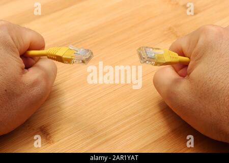 High angle shot of a person holding yellow cables with both hands over a wooden surface Stock Photo