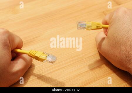 High angle shot of a person holding yellow cables with both hands over a wooden surface Stock Photo