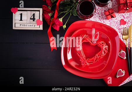 Valentines day dinner with table  setting with gift, red roses, hearts with two wineglasses on dark background. Top view, flat lay. Stock Photo