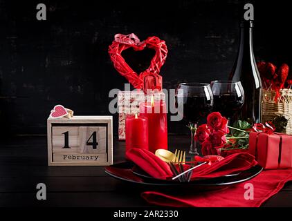 Valentines day dinner with table  setting with gift, red roses, hearts with two wineglasses on dark background. Stock Photo