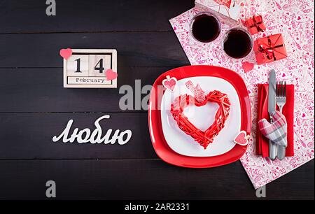 Valentines day dinner with table  setting with gift, red roses, hearts with two wineglasses on dark background. Top view, flat lay. Stock Photo