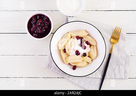 Traditional  ukrainian / russian cottage cheese lazy dumplings served with sour cream and cherry jam on white wooden background. Top view, overhead, c Stock Photo