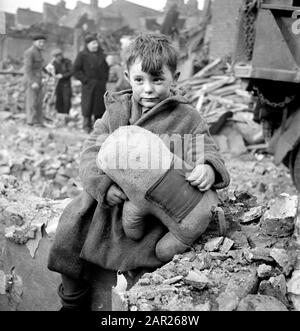 Abandoned Boy holding Stuffed Animal while sitting by Ruins of Building during World War II Bombing of London, England, UK, photograph by Toni Frissell, January 1945 Stock Photo