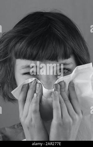 Black and white portrait of a sick child blowing her nose