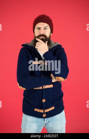 Warm and comfortable. Brutal temper. Fashion menswear shop. Masculine clothes concept. Winter menswear. Clothes design. Man bearded warm jumper and hat red background. Winter season menswear. Stock Photo