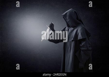 Hooded man with ancient knife in the dark Stock Photo