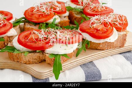 Open sandwiches with fresh mozzarella, tomatoes and arugula. Italian food concept Stock Photo