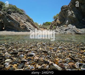 Mediterranean sea small cove on rocky shore with pebbles underwater, split view over and under water surface, Spain, Costa Brava, Cadaques, Catalonia Stock Photo