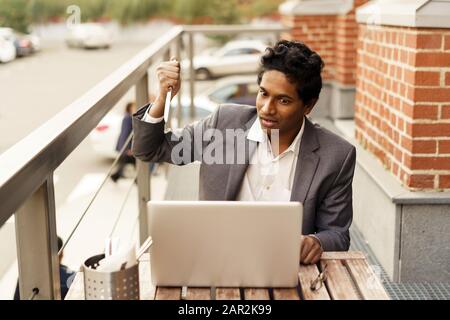 Young handsome Indian man in a summer cafe with a laptop with a table knife Stock Photo