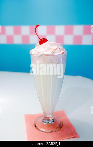 Glass of vanilla milkshake with whipped cream and cherry on blue background in retro cafe