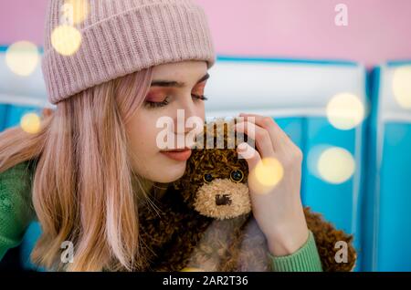Portrait of a pretty girl in green sweater. Beautiful young woman hugging teddy bear. Bokeh lights Stock Photo