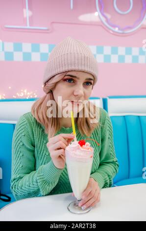 Portrait of a lovely girl in green sweater with milkshake. Hipster girl sitting in cafe Stock Photo
