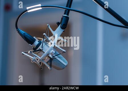 Closeup of a professional condenser microphone mounted on a tripod set up in a concert hall. Silver metal material and black audio cables with bokeh. Stock Photo