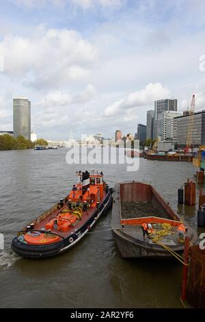 A tug and barge work on a construction project on the Thames river near Vauxhall bridge in London, UK Stock Photo