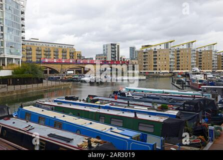 Residential canal boats moored in Limehouse Basin marina in eastern London, London, UK as a Docklands Light Railway Train crosses the viaduct Stock Photo