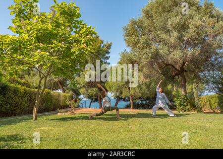 Two women doing yoga warrior pose. Healthy lifestyle. Strong body concept. Happiness concept. Happy mother with daughter spending time outdoor Stock Photo