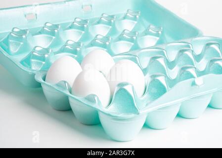 A close-up shot of a polystyrene egg crate with four white eggs set on a plain neutral background. Stock Photo