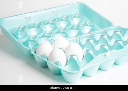 A close-up shot of a polystyrene egg crate with four white eggs set on a plain neutral background. Stock Photo