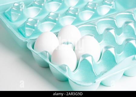 A close-up shot of a polystyrene egg crate with four white eggs set on a plain neutral background. Stock Photo