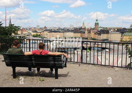 STOCKHOLM, SWEDEN - Aug 02, 2019: Two young men sitting on a park bench, enjoying the beautiful cityscape view of the old Town (Gamla Stan)  of Stockh Stock Photo