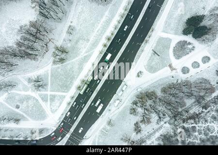 city asphalt road with cars in motion in winter time. suburb area covered with fresh white snow. aerial view Stock Photo