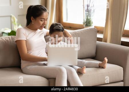 Young Asian mom and daughter using laptop together Stock Photo