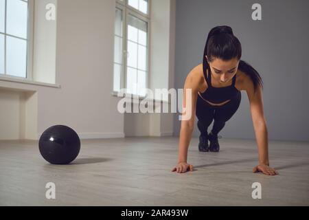 Exercise push ups. Athletic girl in black sportswear doing push-up exercises indoors. Stock Photo