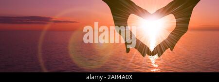 Two hands in the shape of a heart on a sunset background over the sea. The concept of a romantic date, a declaration of love, a love relationship. Stock Photo