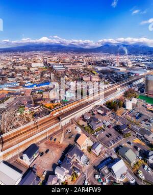 Express trains statin Shin-Fuji in view of famous Japanese Mount Fujiyama on a sunny day - aerial vertical panorama. Stock Photo