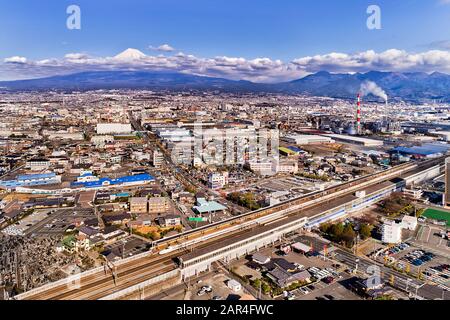 Mount Fuji in Japan under blue sky near Shin-Fuji train station with express passenger train at the platform in elevated aerial view. Stock Photo