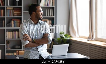 Happy african business man looking away dreaming standing in office Stock Photo