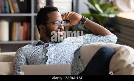 Happy african american man relaxing with laptop looking away dreaming Stock Photo