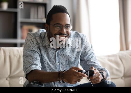 Happy young african guy holding joystick controller playing video game Stock Photo