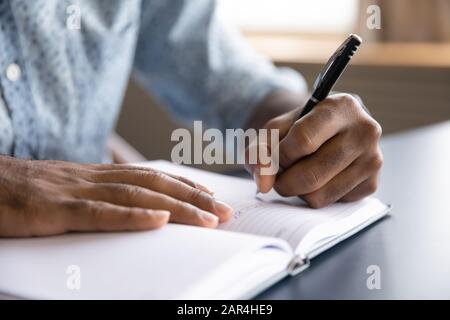 Close up view of african left-handed businessman writing in notebook Stock Photo