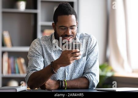 Happy african man using smartphone sit at home office desk Stock Photo