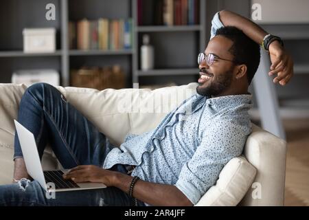 Relaxed african man resting on couch using laptop at home Stock Photo