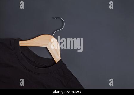 Black t-shirt on wooden hanger lying on black background. Stock Photo