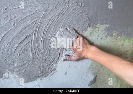 The plasterer Builder puts the plaster on the wall with his hand. Internal construction and finishing works.The hand holds the construction mix and sm Stock Photo