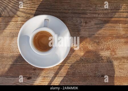 Cup of coffee standing on the wooden e table in sunlight with dropping shadows Stock Photo
