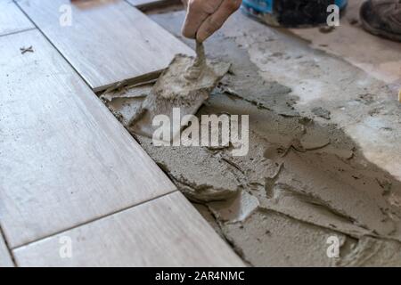 Man installing rectangular shaped floor tiles in kitchen. Applying ...