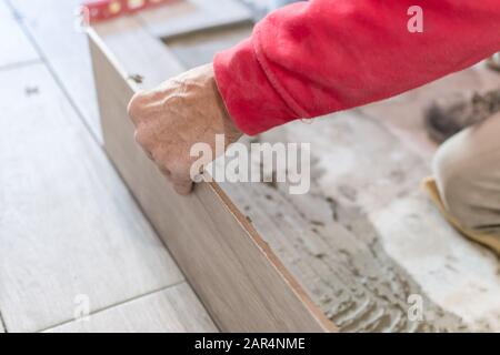 Man installing rectangular shaped floor tiles in kitchen. Applying ...